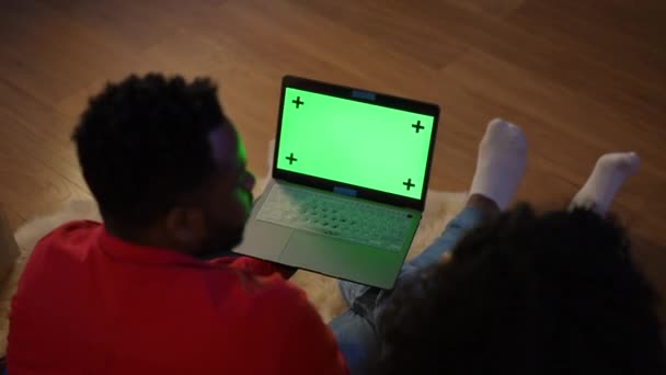 年轻的非洲裔美国人夫妇坐在地板上聊天 手里拿着高角的铬白色笔记本电脑 无法辨认的男女通过绿色屏幕上的社交媒体模板在网上聊天 — 图库视频影像