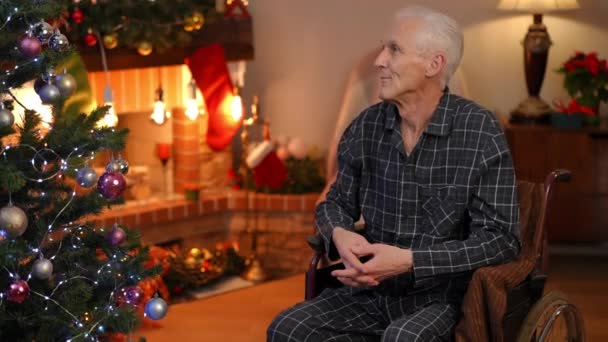 車椅子の幸せなシニア白人男性の交差点の指のクリスマスの前夜に居心地の良いリビングルームに座って目を閉じて話しています 家で新年に願い事をする退職希望の肖像 — ストック動画