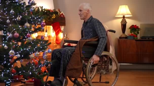 大镜头老年人滚动轮椅到圣诞树调整新年玩具 有信心的白人退休人员在家里客厅里享受节日准备的侧景画像 — 图库视频影像