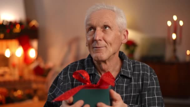 特写快乐的老人 带着新年礼物闭上眼睛 祝圣诞前夜有奇迹 白人男性退休人员在家中舒适的客厅里庆祝节日的画像 — 图库视频影像