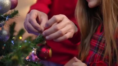 Son sınıf erkek eli Noel ağacına yeni yıl oyuncağı asıyor ve genç kadın avuç içi süslemesi yapıyor. Tatil arifesinde evi dekore eden beyaz büyükbaba ve torun.