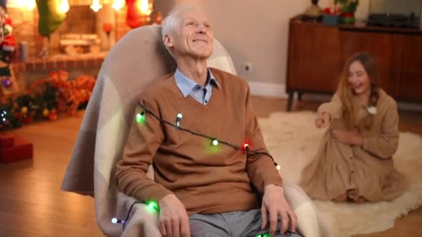 Χαμογελώντας Καυκάσιος Παππούς Κάθεται Κουνιστή Καρέκλα Τυλιγμένο Γιρλάντα Πρωτοχρονιάς Θολή — Αρχείο Βίντεο