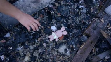 Ukrayna 'nın bombalanmış şehrinde yerden pembe oyuncak toplayan bir kadın. Tanımlanamayan zayıf Ukraynalı kadın yanmış harabe evde kayıp oyuncak topluyor.