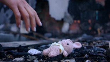 Yakın plan kadın eli bombalanmış yerdeki küllerden ağır çekimde pembe tığ işi oyuncak topluyor. Ukrayna 'da yanmış harabe bir evde tanınmayan genç, zayıf bir kadın.