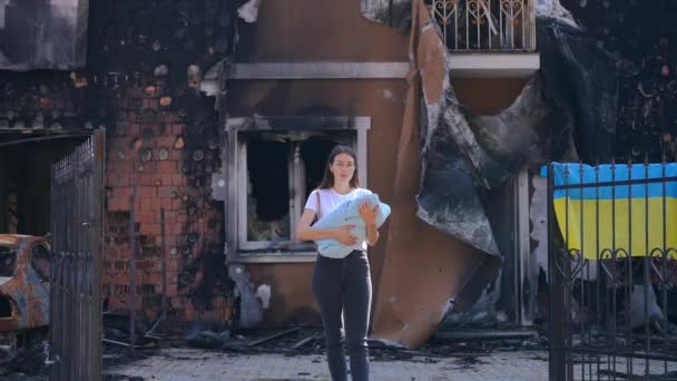 站在被炸毁的室外房屋前 年轻的乌克兰母亲摇摇晃晃地铺着婴儿被子 烧毁的城市里绝望的带着孩子的妇女的正面画像 看着相机 — 图库视频影像
