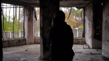 Harap olmuş bir binada duran ve sonbahar günü etrafa bakınan genç bir kadının arka plan silueti. Ukraynalı kadın Ukrayna 'nın Kyiv banliyösündeki yıkılmış evinde. Yavaş çekim