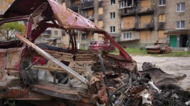 Dışarıdaki harabe konut binasının arka planında kurşun delikleri olan yanmış araba artıkları. Otomobili parçalamış ve Kiev Ukrayna 'daki sivil evi yok etmiş. Yavaş çekim kaide çekimi