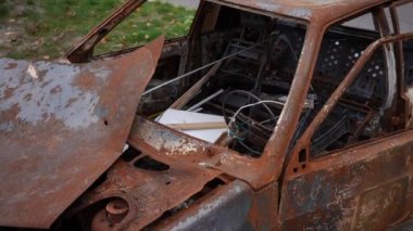 Ukrayna 'nın Kiev banliyösündeki sokakta bombalanmış araba. Yüksek açılı, paslı, camları kırık ve kaputu parçalanmış bir araç. Yavaş çekim