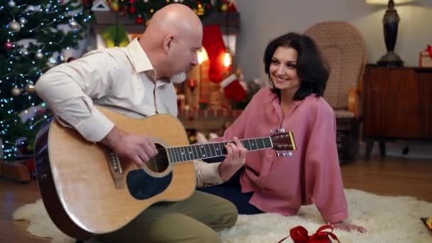 新年の歌を歌う男性としてセレナーデを聴いている幸せな妻は自宅で前夜 広いショットリラックスした正の白人男性と女性一緒にクリスマスのお祝いを楽しんで — ストック動画