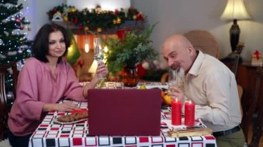 Online kadeh tokuşturan neşeli beyaz çift yemek masasında dizüstü bilgisayarlarıyla oturuyor. Evde Noel 'i kutlayan olumlu karı koca mesajlaşmaları. Tatiller ve kolaylıklar