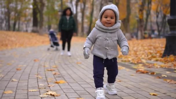 前景色正面 小孩在公园小巷里散步 母亲在后面走来走去 脸上带着模糊的笑容 兴奋的非洲裔美国人孩子在户外享受休闲 — 图库视频影像