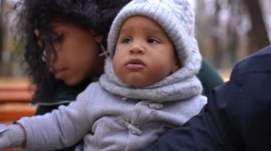 Sonbahar parkında, sevgi dolu bir erkek ve kadının çocuk yanaklarını öptüğü sevimli bir çocuğun portresi. Dertsiz, mutlu, Afro-Amerikan bir çocuk. Ailesi dışarıda dinleniyor.