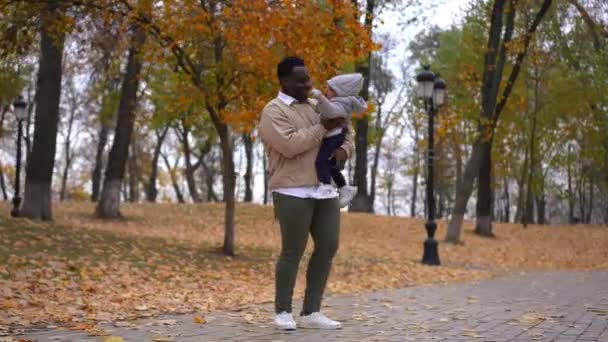 宽阔拍摄快乐的年轻父亲与儿子在秋天的公园里嬉笑 非裔美国人旋转的孩子把孩子放在小巷里和男孩一起走 — 图库视频影像