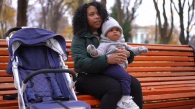 Sonbahar parkında ailesiyle birlikte kadının kucağında oturan tatlı küçük çocuk. Afro-Amerikalı çocuk annesiyle dışarıda eğleniyor.