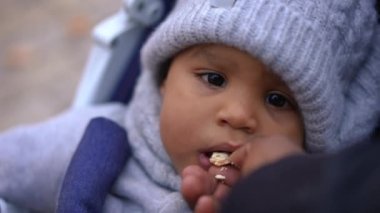 Vesikalık fotoğraf, bebek arabasındaki tatlı Afro-Amerikan çocuk ve kadın eli ekmeği ile besleyen çocuk. Kaygısız çocuk portresi dışarıda çörek yiyor tanınmayan bir anneyle dinleniyor.