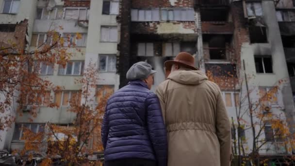 戻るウクライナの街で屋外に立って話している荒廃した住宅建築物を見ている高齢者のカップルを表示します 失われた財産を議論する古い白人男性と女性 ロシア ウクライナ戦争の概念 — ストック動画