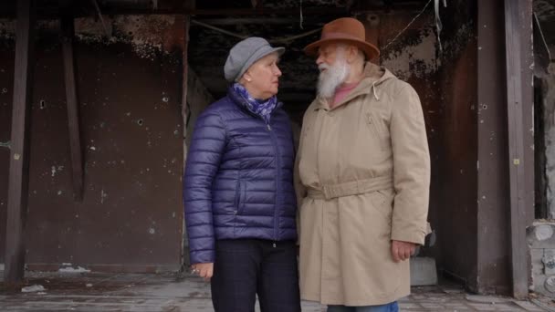 沮丧绝望的老夫妇站在被轰炸的乌克兰城市住宅大楼被毁的入口交谈 在被毁的城镇里 伤心的男人和女人在户外沮丧地等待着 慢动作 — 图库视频影像