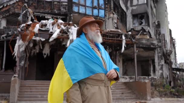 严肃而悲伤的老人 肩膀上挂着乌克兰国旗 望着远方 一边想着镜头在镜头前放大 在被炸毁的城市里沮丧绝望的退休人员的侧角画像 — 图库视频影像
