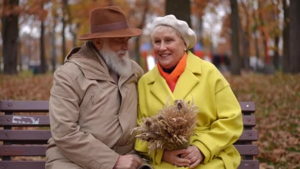 Sonbahar Parkında Bankta Buğday Buğdayıyla Oturmuş Gülen Pozitif Yaşlı Çift — Stok video