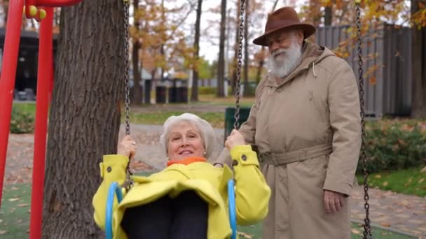 Lächelnder Älterer Mann Schaukelt Entspannt Frau Auf Schaukeln Auf Kinderspielplatz — Stockvideo