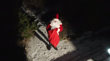 Noel Baba arka bahçede karanlıkta yürüyor ve verandaya Noel hediyesi koyuyor. Kırmızı kostümlü beyaz adamın yüksek açılı portresi. Yeni yıl gecesi dışarıda sürpriz yapıyor.