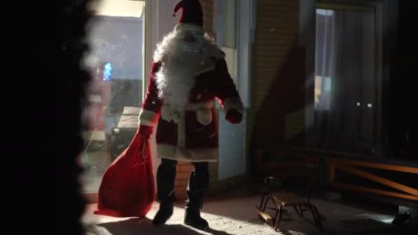 サンタは新年の暗い裏庭の家から重いギフトバッグを引っ張って歩く クリスマスの夜の屋外での休日の贈り物と白人男性の肖像画 お祝いと奇跡の概念 — ストック動画