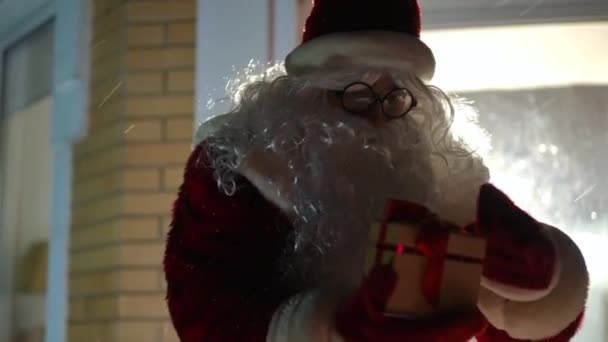 在外面的雪夜 身着圣诞老人服装的白人男子的中景肖像打开礼品盒 里面点着光 惊讶的家伙 满脸兴奋的回头看门 — 图库视频影像