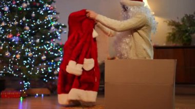 Beyaz adam, Noel Baba ceketini karton kutuda paketliyor oturma odasında yeni yıl ağacıyla oturuyor. Noel kutlamasından sonra evde genç bir adamın portresi. Yaşam tarzı ve tatil konsepti