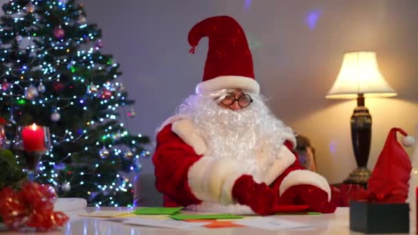 Συγκεντρωμένος Άγιος Βασίλης Κάθεται Στο Τραπέζι Διαβάζοντας Γράμματα Πολύχρωμο Χαρτί — Αρχείο Βίντεο