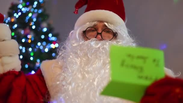 一个穿着圣诞老人服装的人 把眼镜放下 坐在屋里看书 圣诞前夜 在圣诞树下 一个专心致志的男人的画像 希望与奇迹 — 图库视频影像