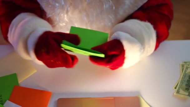 表に座ってノートパソコンのキーボードを入力して文字で認識できないサンタを表示します 赤いスーツの男と願いをオンラインで作る贈り物を注文するミトンが実現します 新年とクリスマスの奇跡 — ストック動画
