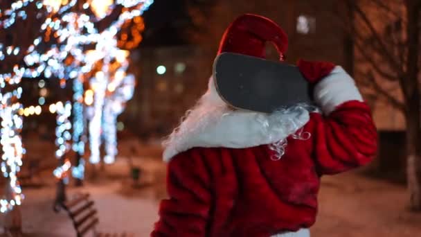Ein Mann Weihnachtsmannkostüm Mit Skateboard Steht Nachts Draußen Und Schaut — Stockvideo
