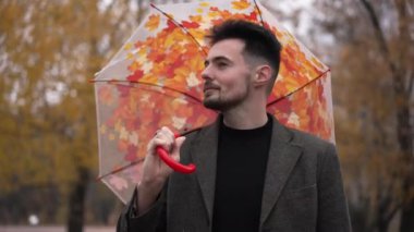 Kamerayı katlayan şemsiyeye bakıp etrafa gülümseyen yakışıklı bir adam. Mutlu, rahat, Kafkasyalı adam parkta sonbahar tatilinin tadını çıkarıyor. Huzur ve yaşam tarzı