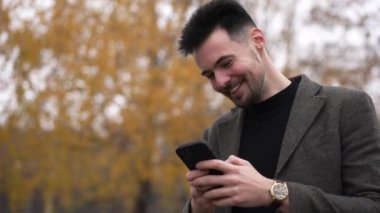 Genç, mutlu bir adam, sarı ağaç kaplamasının sağında duran akıllı telefon uygulamasında yüksek sesle mesajlaşarak gülüyor. Ormanda dinlenen tasasız, tasasız, beyaz bir adamın portresi.