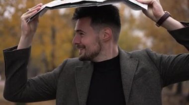 Sonbahar parkında yağmurlu bulutlu bir günde elinde kağıt harita tutan neşeli beyaz adam. Kendine güvenen neşeli turistin portresi. Dışarıya bakınmaktan keyif alıyor.