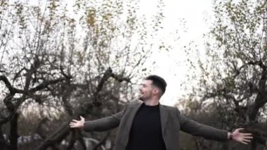 Gülümsemenin portresi beyaz yakışıklı genç adam ellerini uzatıyor ve sonbahar tatilinin tadını çıkarıyor. Bulutlu gökyüzünün arka planında duran kendine güvenen zarif adamın ön görüntüsü.