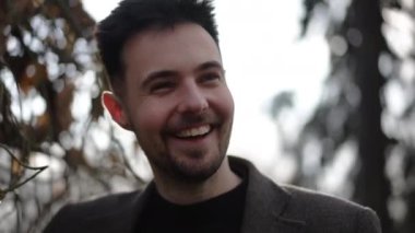 Açık havada gün ışığında gülen neşeli genç adamın portresi. Kafkas çağının yakın çekimlerinde, sonbahar tatilinin tadını çıkaran parktaki arka ışıklandırmalı güneş ışığının tadını çıkaran adam.