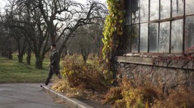 Geniş açı pozitif milenyum adamı sonbahar parkında sokakta yürüyor. Gülümseyen yakışıklı beyaz adam cam binanın önünden geçiyor dışarıda geziniyor. Yaşam tarzı kavramı