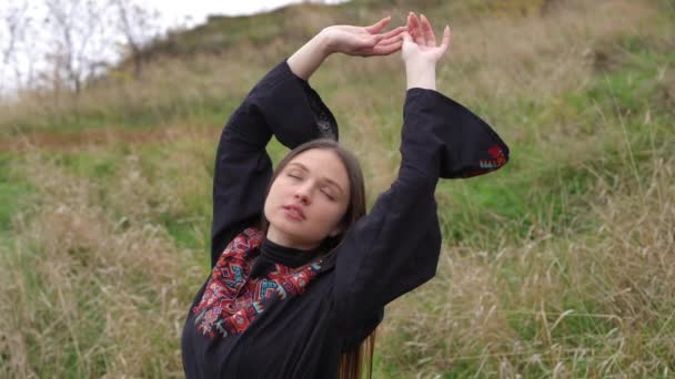 穿着黑色绣花衣服的年轻貌美的女子站在室外慢动作地举手 在阴天 自信美丽的乌克兰女士在秋天的田野里享受着宁静 — 图库视频影像