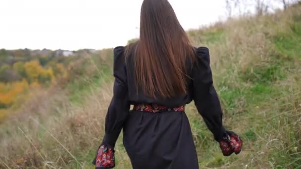 身穿黑色衣服 头戴乌克兰传统刺绣的年轻女子站在山顶上向后看 秋天的阴天 松懈的女士在户外散步 享受宁静的闲暇 — 图库视频影像
