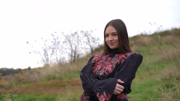 在阴沉沉的日子里 向站在户外欣赏秋天河流的自信微笑的年轻女子看齐 穿着黑色绣花衣服的快乐迷人的乌克兰女士 梦想着享受休闲 — 图库视频影像