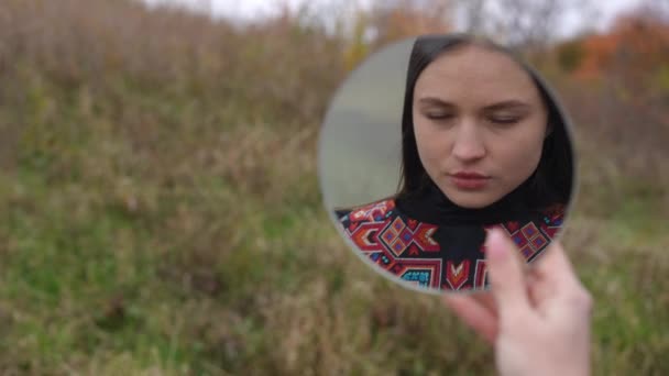 在多云的日子里 站在秋天田野上自信而华丽的乌克兰女子的近照映照在手中 外面穿着民族服装的漂亮迷人的黑发姑娘 — 图库视频影像