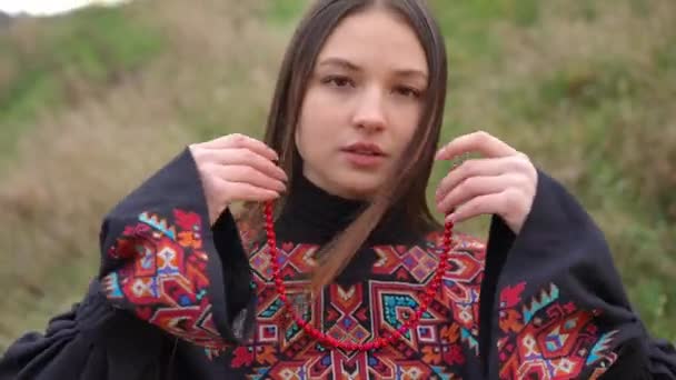 迷人而自信的年轻女子穿着红珍珠项链看着镜头的正面肖像 穿着绣花的乌克兰传统服装在户外摆出一副美丽的女士的模样 — 图库视频影像