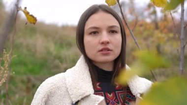 Büyüleyici genç bayan, sonbahar günü dışarıda dikilirken yüzünü kaçırmayı hayal ediyor. Kendine güveni tam beyaz bir kadının portresi. Önünde ağaç dallarıyla sahada huzurun tadını çıkarıyor.