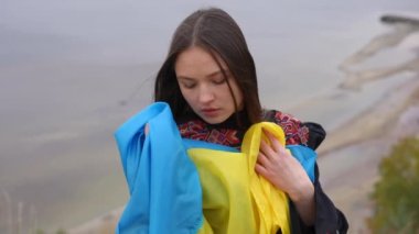 Ulusal bayrağı olan Ukraynalı genç bir kadın nehir kıyısının arka planında kameraya bakıyor. Nakışlı elbiseli güzel esmer kadının portresi ağır çekimde poz veriyor.