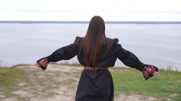 ビュー興奮した若い女性が遅い動きで川に秋の日に屋外で手を伸ばし実行している 幸せな自信を持ってウクライナの女性で刺繍黒ドレス楽しんでレジャー — ストック動画