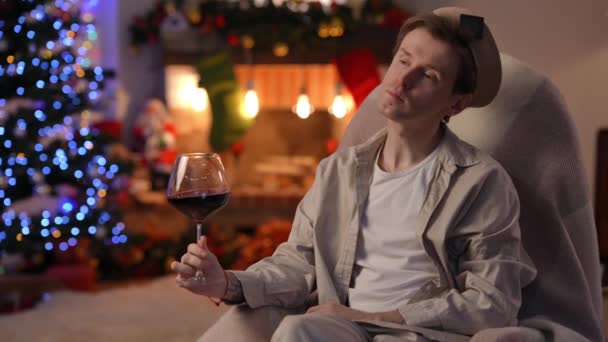 自信を持った男は赤ワインの右側の揺れガラスの上に椅子ロックに座ってお酒のにおい 集中白人Lgbt男おいしい飲み物とともに自宅で新年の前夜にクリスマスを祝う — ストック動画