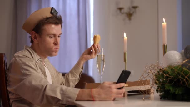 サイドビュー退屈男はクリスマスディナーテーブルで左側に座ってピザを食べるスマートフォンアプリでソーシャルメディアをスクロールします 中出しの白人Lgbt男祝う休日一人で家に — ストック動画
