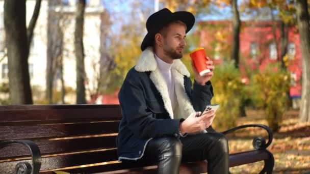 Uśmiechnięty Człowiek Lgbt Pijący Wiadomości Kawie Aplikacji Smartfona Siedzącej Ławce — Wideo stockowe
