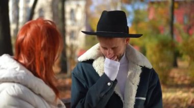 Güneşli bir günde, alnına dokunan endişeli bir kadınla hapşıran yakışıklı genç adamın portresi. Sonbahar parkında endişeli bir annesi olan zarif LGBT oğlu. Bakım ve sağlık kavramı